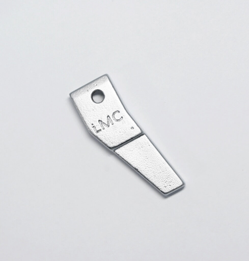 Small silver metal blade-shaped tool with a circular hole near the top and 'LMC' engraved on it